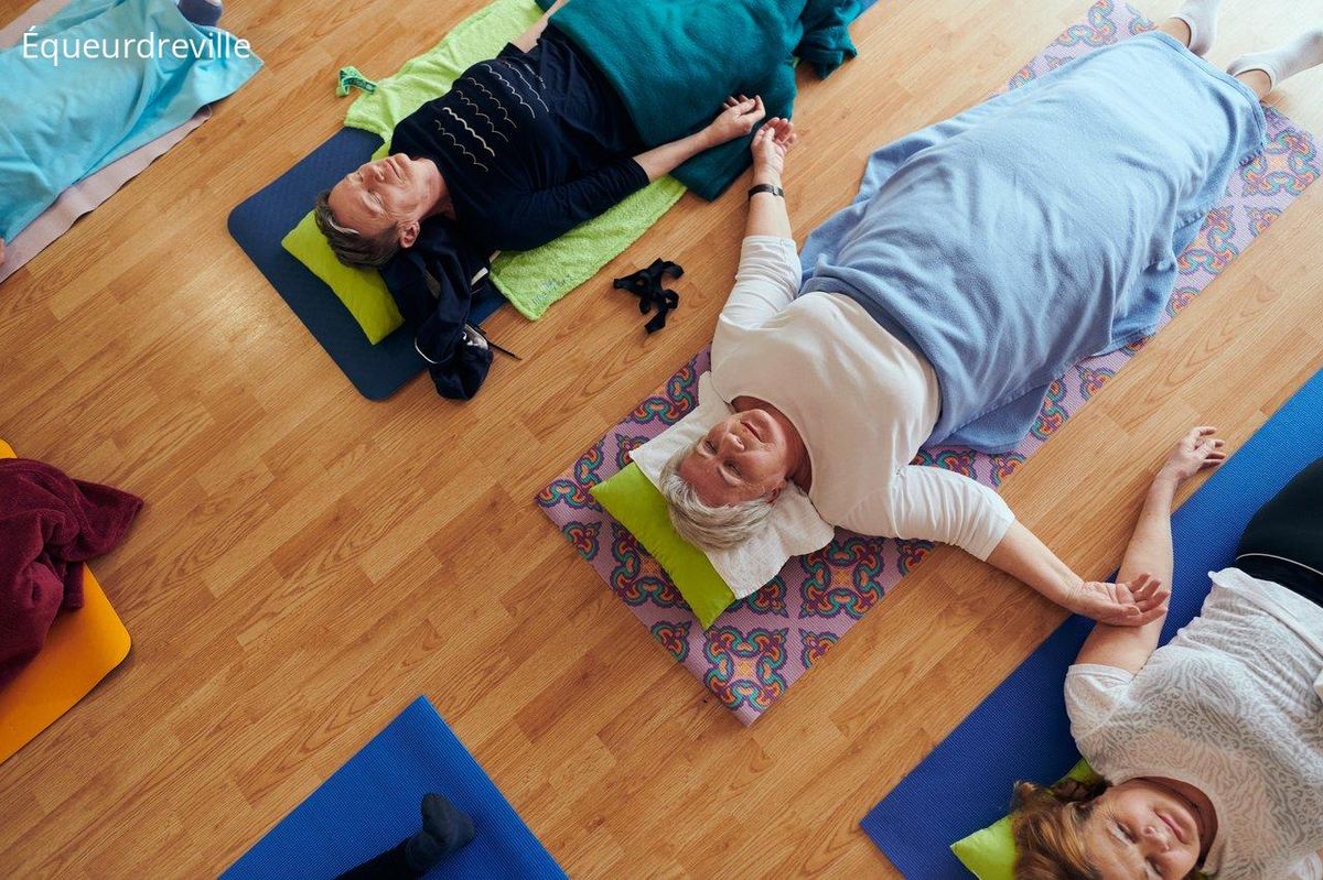 Groupe de seniors pratiquant le yoga en groupe dans une salle lumineuse pour leur bien-être.