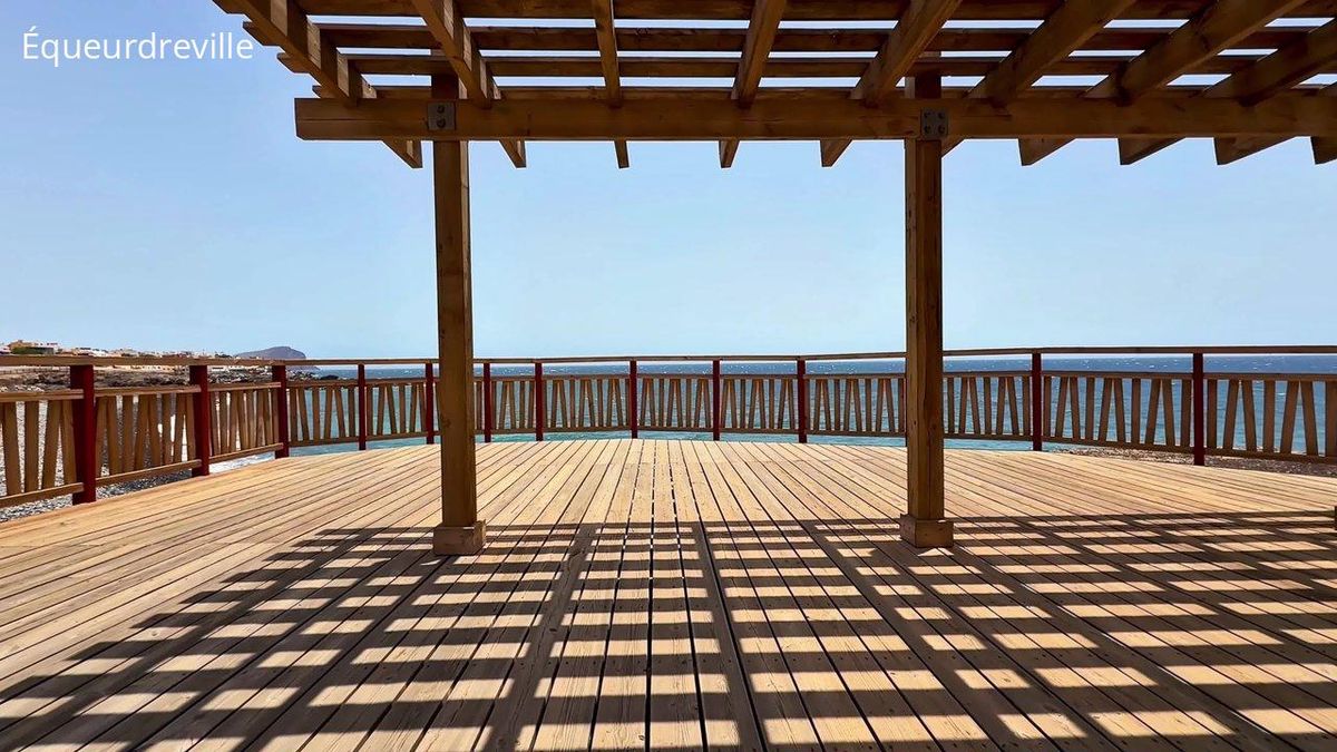 Terrasse équipée d'une pergola bioclimatique en bois offrant une vue imprenable sur l'océan.