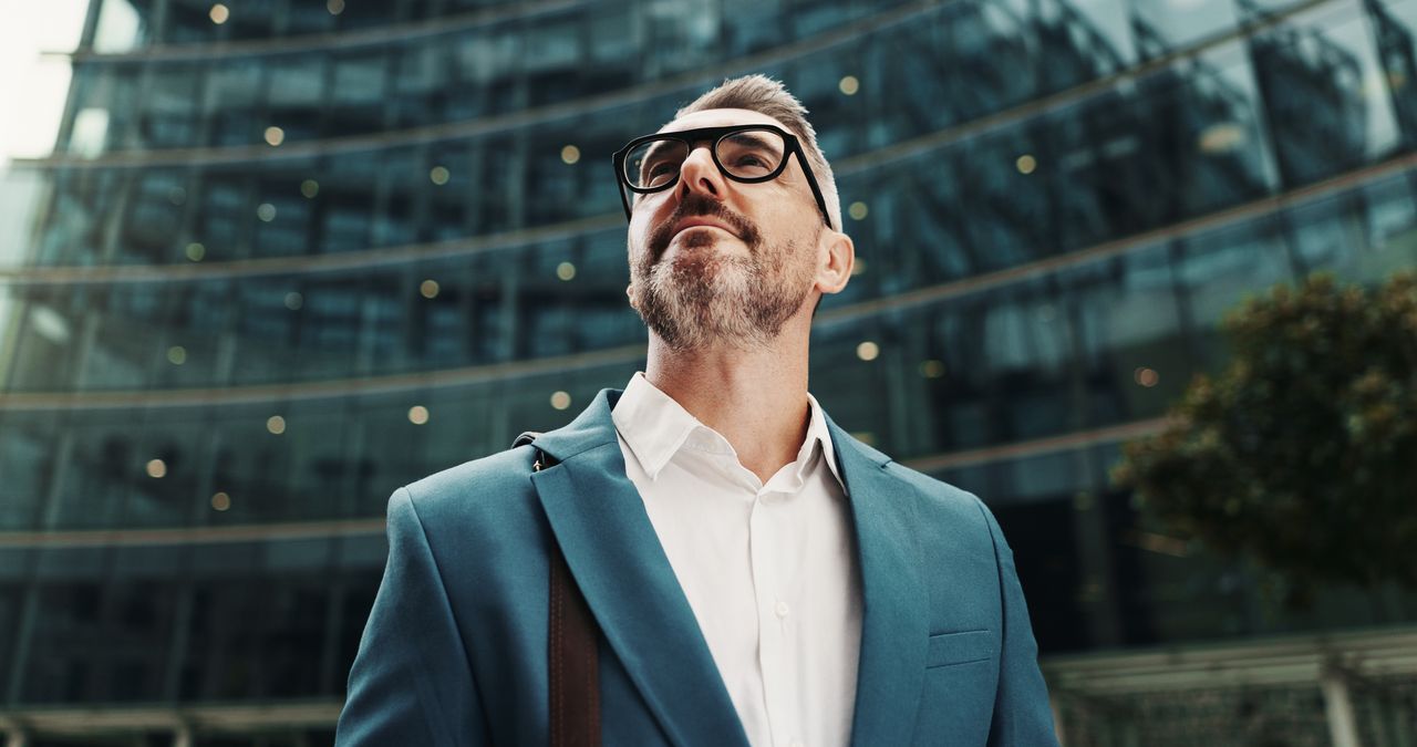 Homme d'une quarantaine d'années, chemise sobre, lunettes fines, expression attentive, photographié devant des façades commerçantes de centre-ville