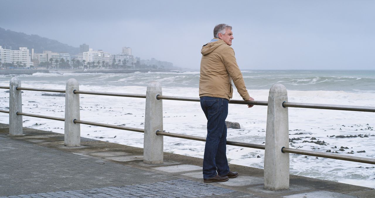Homme d'une cinquantaine d'années aux cheveux gris courts, veste en tweed, sourire discret, photographié sur un quai du port avec la rade de Cherbourg en arrière-plan